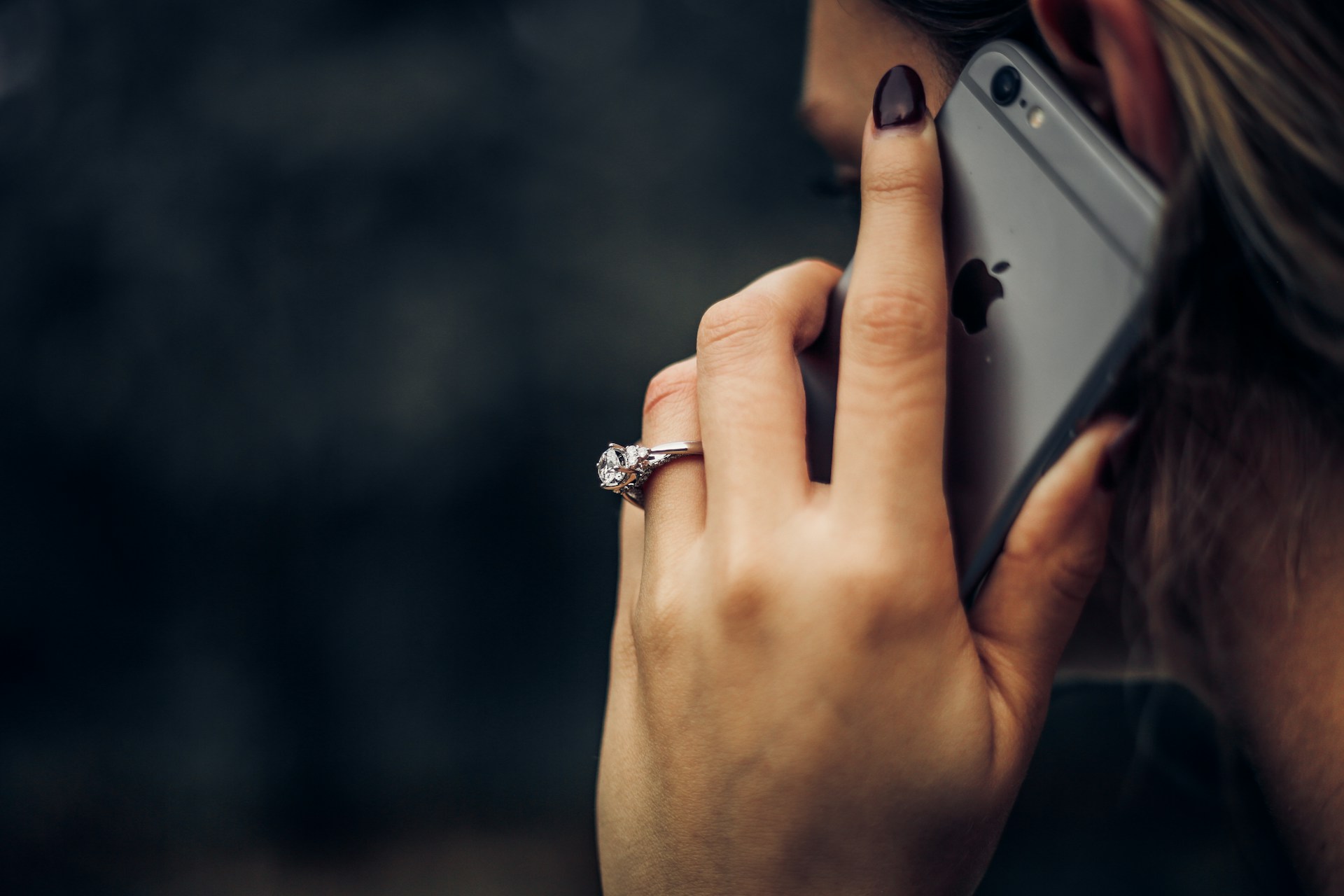 Eine Frau telefoniert mit dem Smartphone. Ihr Gesicht ist der Kamera abgewandt. Im Hintergrund ist es dunkel.