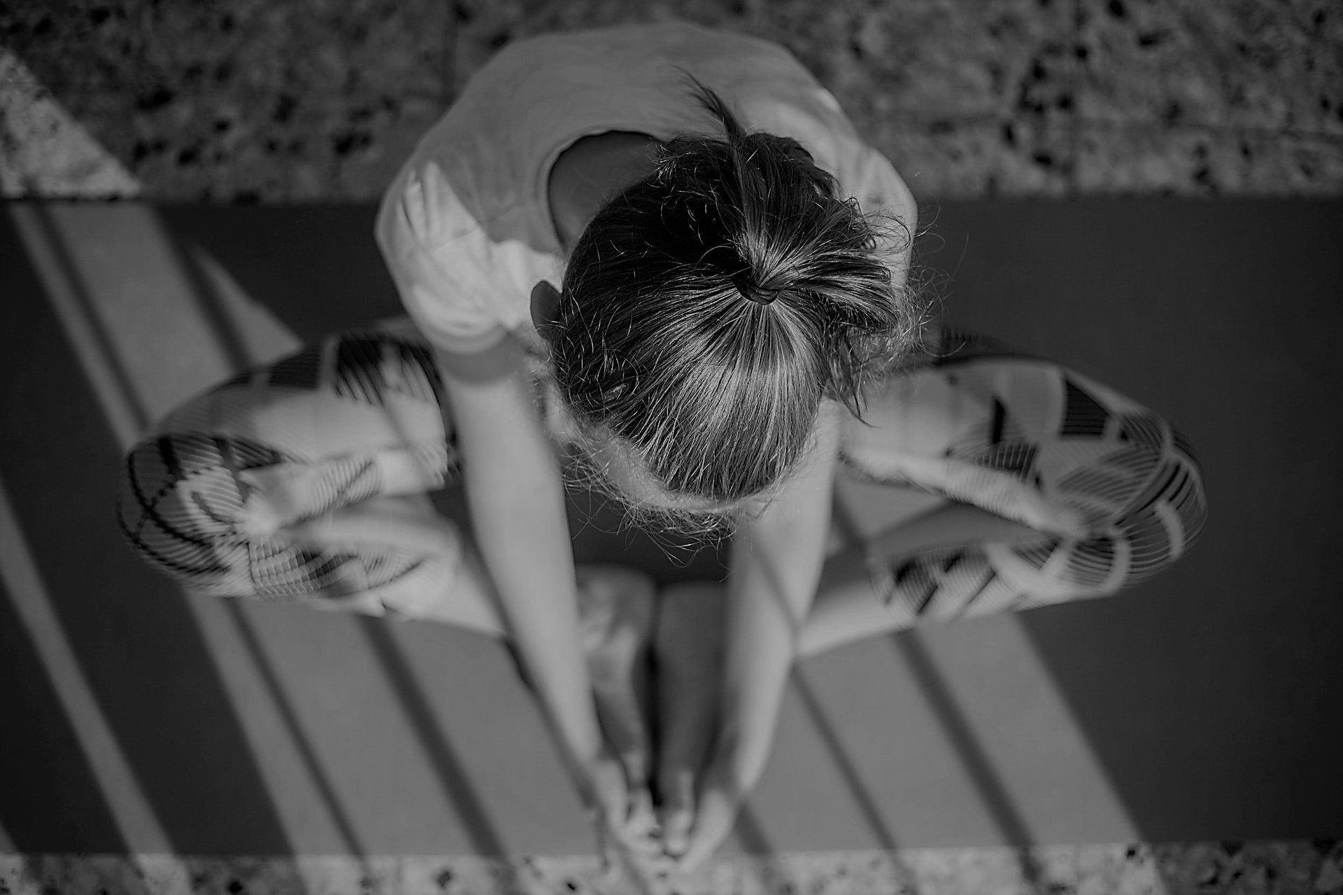 Eine Frau sitzt auf einer Yoga-Matte und umfasst ihre Füße mit ihren Händen